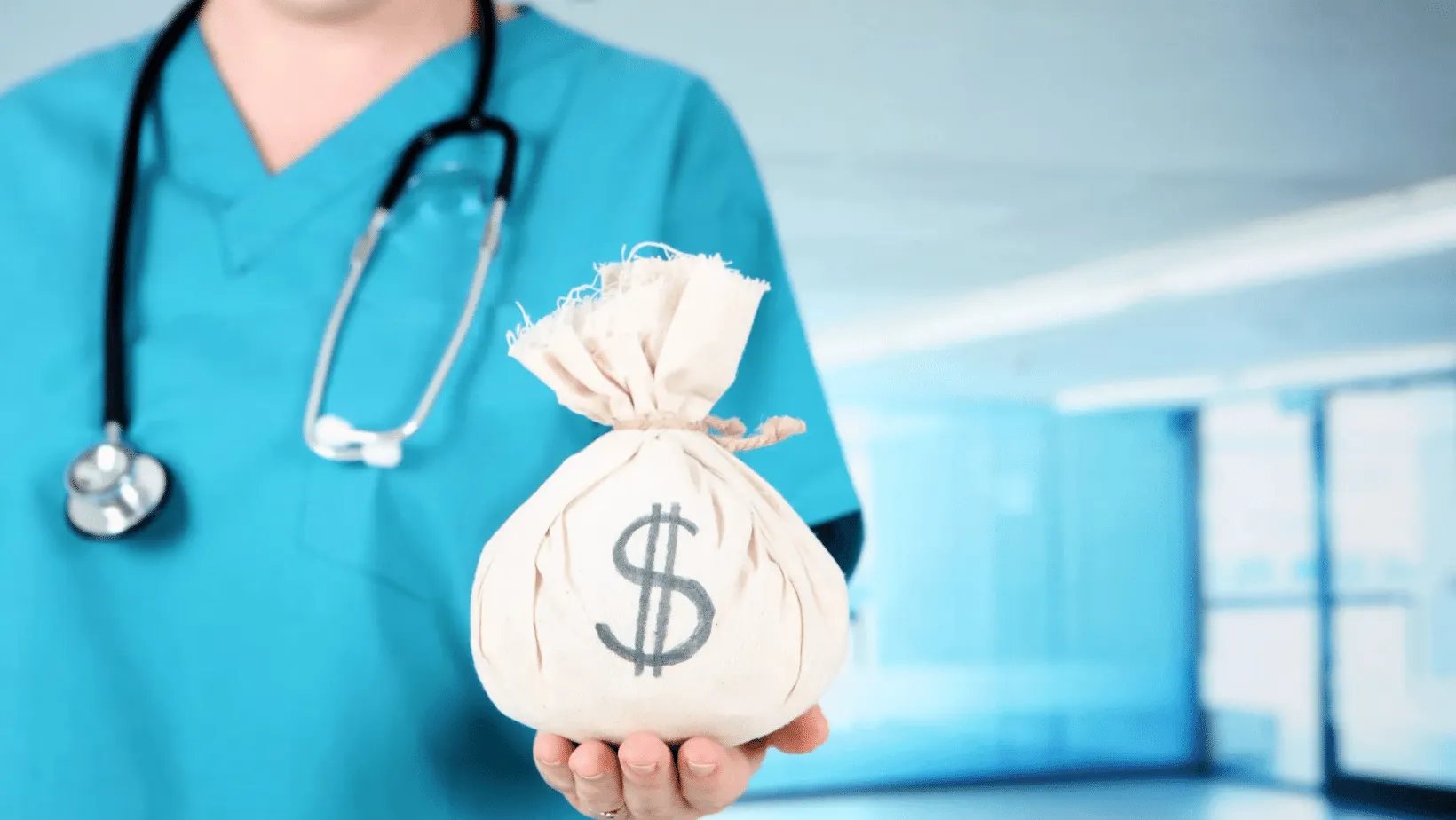 A healthcare professional in blue scrubs holding out a money bag with a dollar sign, symbolizing the financial aspects of healthcare, in a hospital corridor.